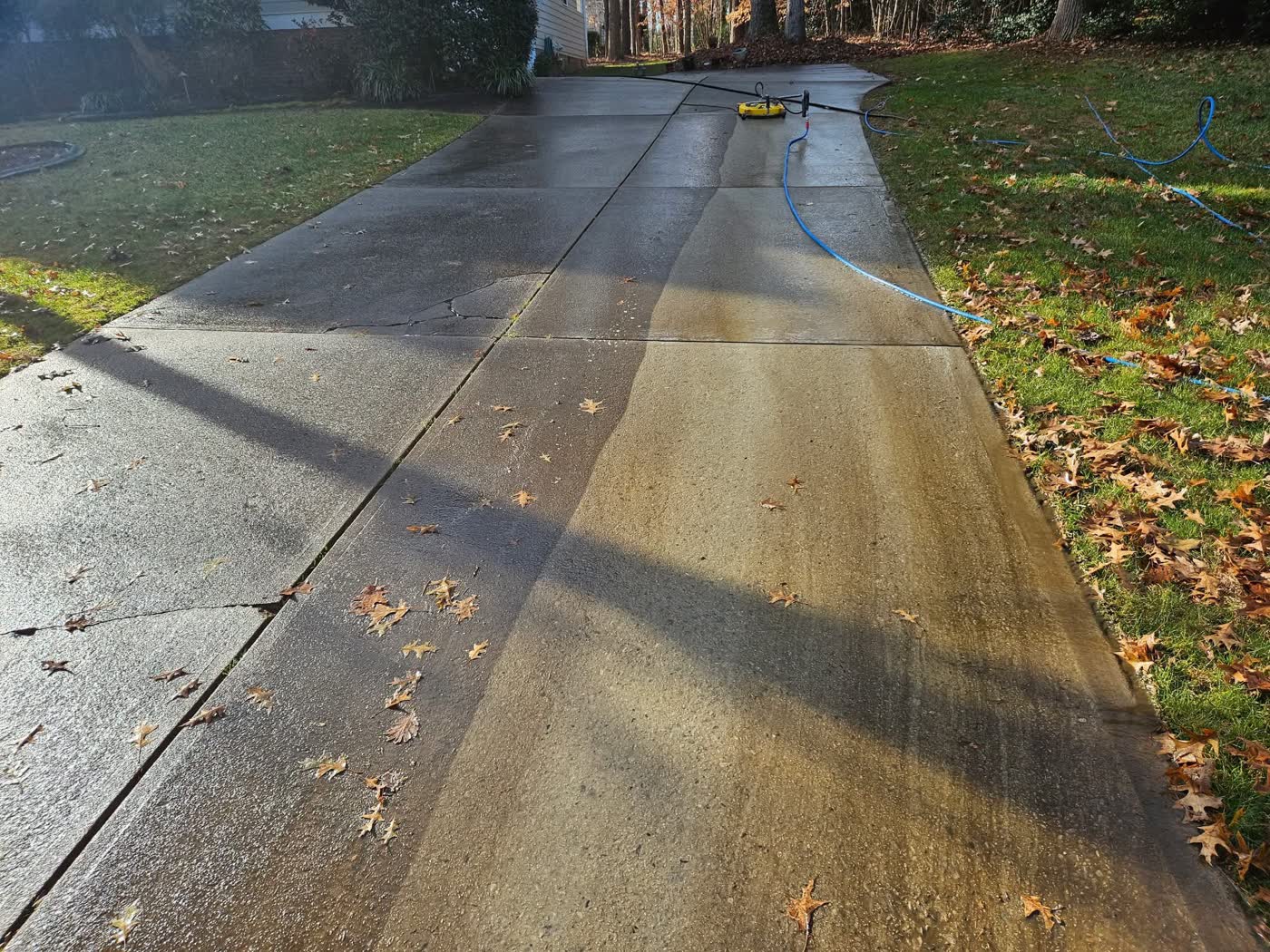 Concrete driveway mid-clean showing the sharp line a surface cleaner leaves